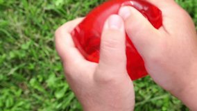Two hands firmly squeeze the bright red anti -storm, a slime above green grass, stretching the surface to the break, when transparent water breaks in daylight. ASMR - Powered by Shutterstock - Get 15% off with code: PIKWIZARD15