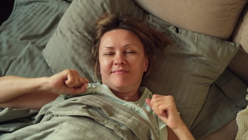 Middle age woman is waking up, stretching arms at bedroom