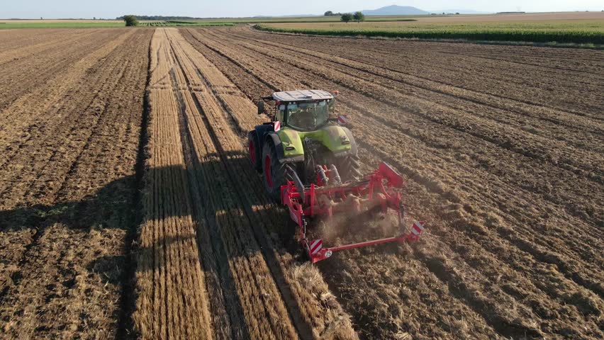Modern tractor working on farmland, cultivating soil after harvest. Tractor plowing agricultural field. Concept of agriculture, harvest and farming machinery