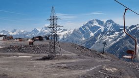 Scarlet chairlift ascending rocky mountain terrain, passing electricity pylon, revealing snow-capped peaks and sweeping wilderness under azure sky - Powered by Shutterstock - Get 15% off with code: PIKWIZARD15