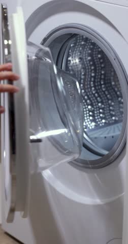 woman with basket doing laundry at home, female hand loading colour laundry into the drum of washing machine.