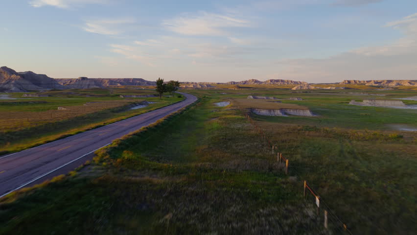 A road snakes through jagged Badlands, captured at glorious sunset as warm light highlights the rugged terrain and vivid skies create a breathtaking natural landscape scene