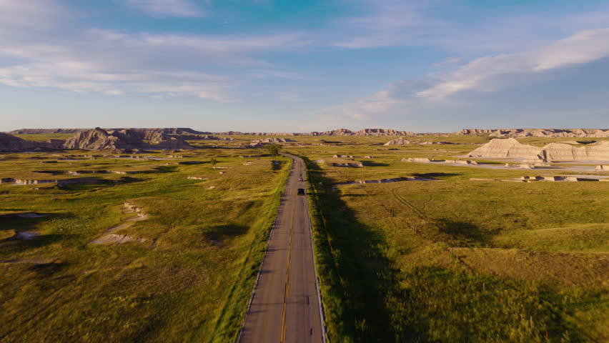 Golden light shines on a rugged Badlands road in a stunning aerial view, highlighting dramatic terrain, winding paths, and the natural beauty of this remote landscape at sunset