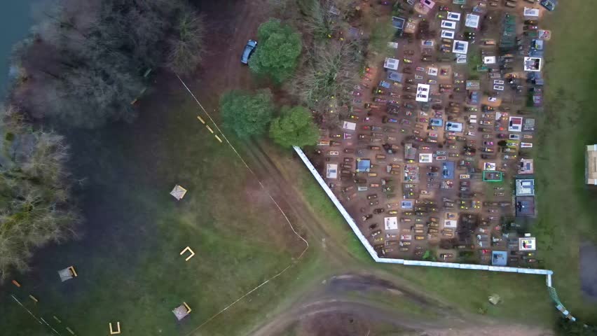 Drone pans and elevates over a Catholic church with a light roof, a cemetery with flowers and markers, and green fields in Belarus.