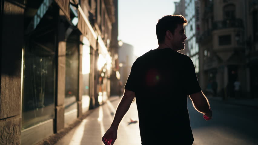 Silhouette of man walking through city street at sunrise with strong shadows. Represents reflection, balance, and vitality in modern urban lifestyle