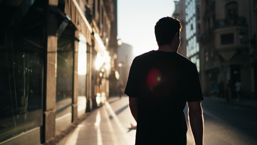 Silhouette of man walking through city street at sunrise with strong shadows. Represents reflection, balance, and vitality in modern urban lifestyle