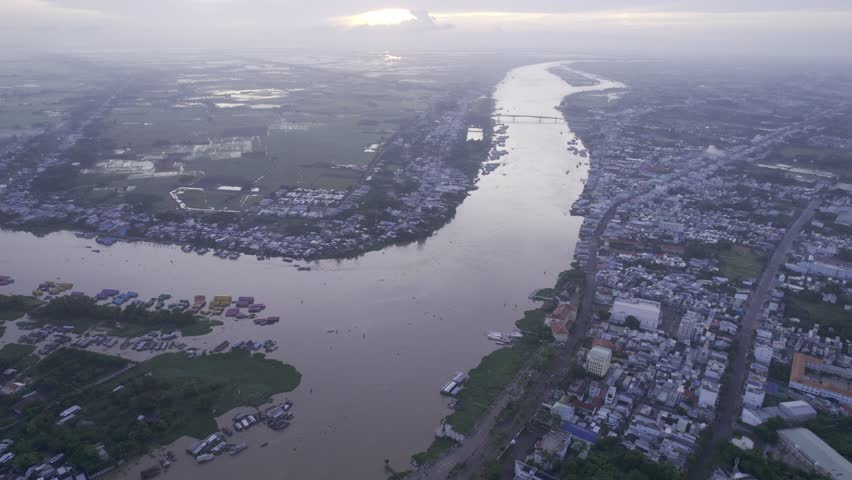 Drone footage capturing a magnificent sunrise over the Chau Doc river, a highlight of any trip to the Mekong Delta. The expansive aerial view reveals the sprawling landscape where the river winds thro