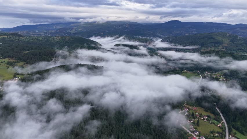 Scenic aerial view of foggy mountain valley with hidden village roads under clouds, captured in cinematic motion from left to right