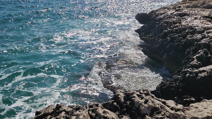 White waves crash against sunlit rocks, the sea sparkling under the summer sky, an escape where time slows and every breeze whispers freedom