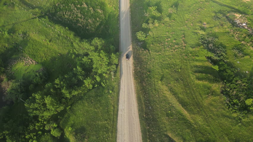 Black sedan driving along twisting rural road, passing verdant farmland with sweeping crop fields extending toward far-reaching skyline