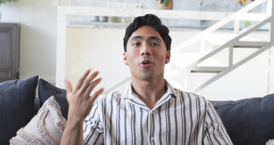Sitting man wearing striped shirt on sofa in modern living room, with pillows and staircase. Lifestyle, interior, contemporary, relaxation, casual, home decor, comfort