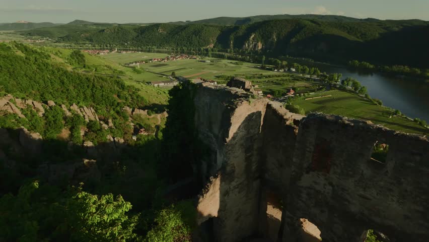 Scenic view from a high hill in Dürnstein, Austria. Ruins of a medieval stone building in the foreground, vineyards, green hills and the Danube River in the valley.