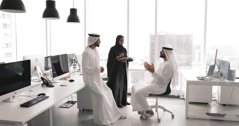 Arabian business team of three standing in circle in open office space, talking in co-working center, discussing teamwork, investment, planning tasks, brainstorming on product development strategy