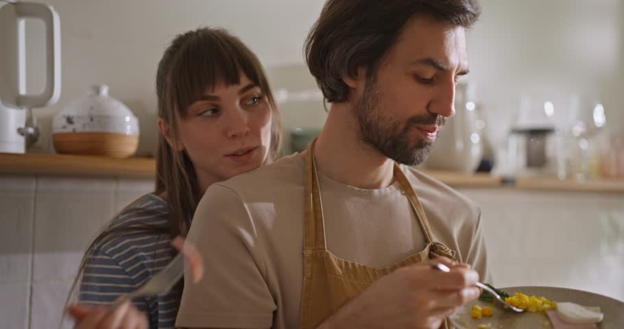 Happy girl feeding her boyfriend delicious breakfast after cooking in the morning in the kitchen hugging and tasting together. Cooking and socializing together at home