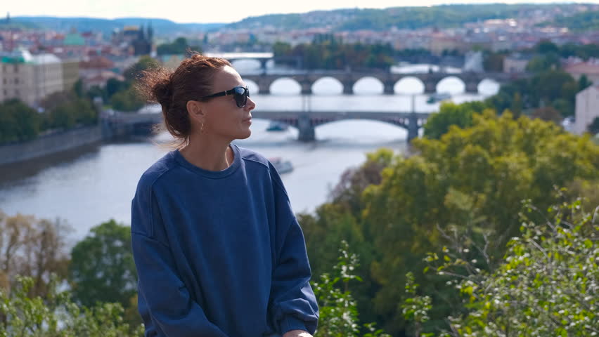Tourist enjoying vltava river view from a park in prague. Young woman standing in scenic park overlooking vltava river, gazing at historic prague cityscape with charles bridge
