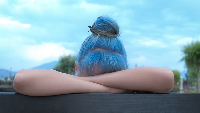 Alone on the bench. A teenage girl hides her face behind a bench in a summer park