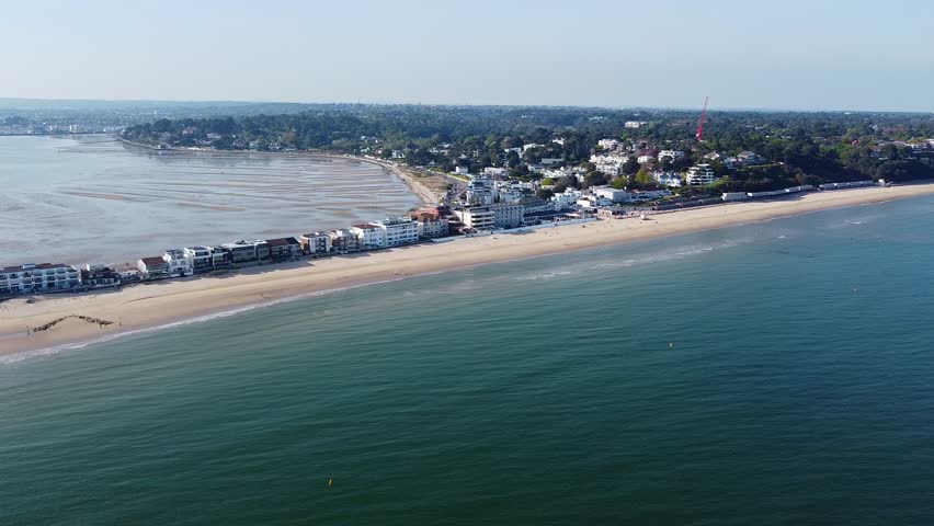Stunning aerial drone footage of Sandbanks Beach in Poole, Dorset, overlooking the coastline, Poole Quay, English Channel. A clear sunny day with sandy beaches, residential buildings, and tranquil sea