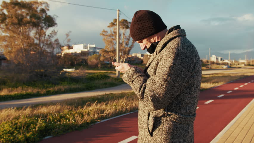 Old Man Scrolling His Smartphone Under the Winter Sun 