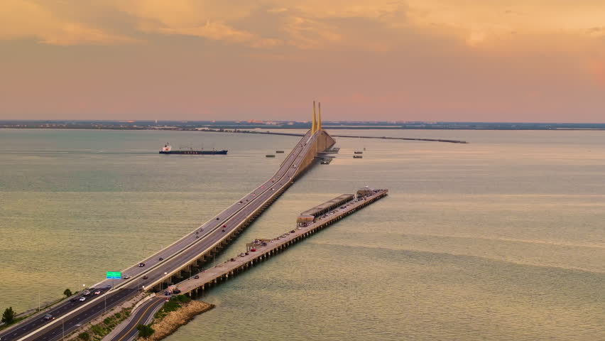 Transportation infrastructure of Florida, USA. Sunset above Sunshine Skyway Bridge over Tampa Bay with driving traffic cars and fishing pier