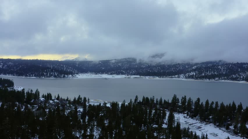 Winter in Big Bear Lake, CA. Orbit around trees and lake and mountains during sunset.
