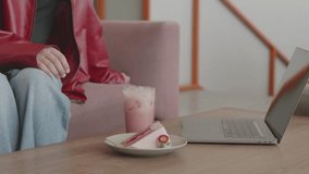 Close-up of woman’s hand reaching for a slice of strawberry cake on a plate next to a laptop and pink iced drink, seated in a cozy modern cafe or coworking space. - Powered by Shutterstock - Get 15% off with code: PIKWIZARD15