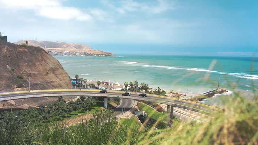 Traffic flows on a bridge over a coastal highway in lima, peru, with the pacific ocean in the background