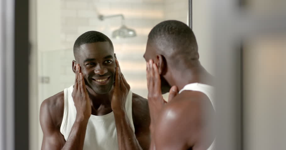 Examining jawline African American man wearing tank top in bathroom, with mirror and shower head. Skincare, grooming, masculinity, modern, wellness, interior, healthy