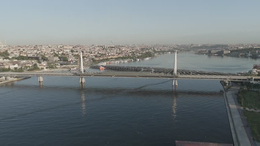 D-Log M. Istanbul, Turkey. Golden Horn Bridge and Halic Metro Station with pedestrian crossing illuminated by morning sun over bay, Aerial View, MasterShots, Dronie