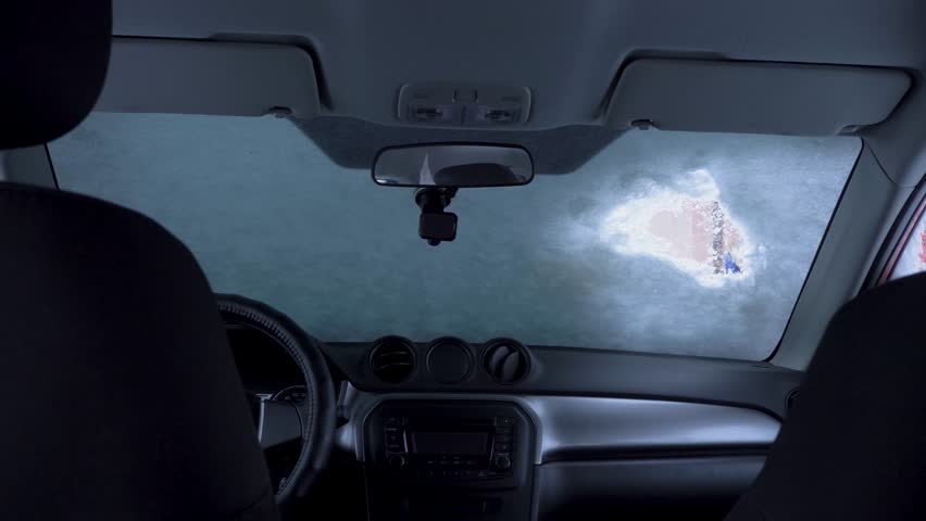 Shovelling snow off car in winter. Scraping ice. Scraping ice from car windows in winter. Brush snow and ice off car windows. View from inside the car