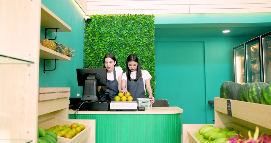 Caucasian and Asian LGBTQ couple working together behind tropical fruit shop counter preparing store for business opening with cooperation and partnership