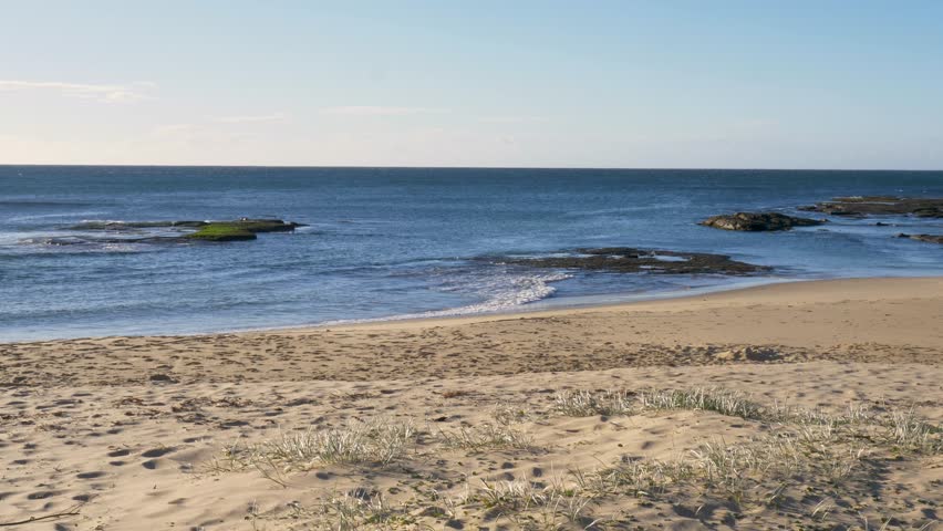 Slow motion landscape of small ocean waves breaking on a sandy beach shoreline with rocky reef formations along the coastline headland point of Bateau Bay Central Coast Australia travel tourism nature