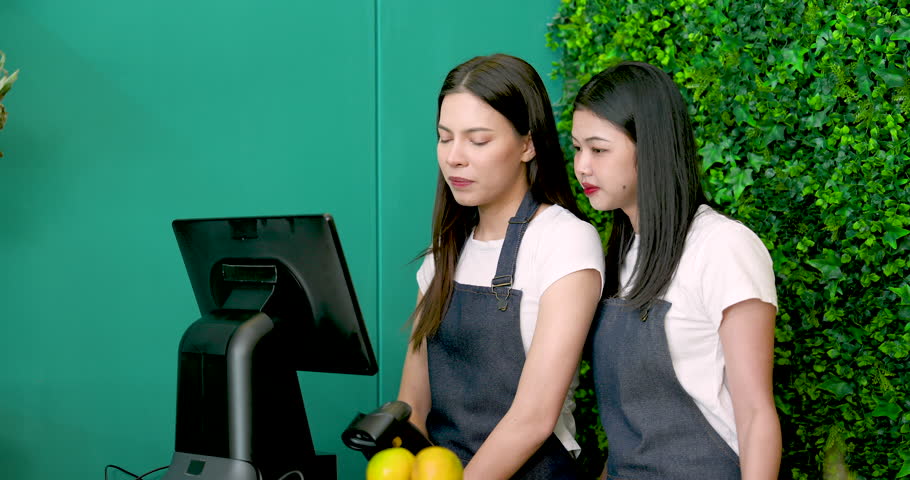 Caucasian and Asian LGBTQ business partners discussing at checkout point while preparing tropical fruit store before morning opening as small retail owners