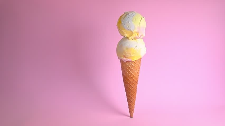 Standing wafer cone topped with vibrant two ice cream scoops, adorned with colorful sprinkle shower against soft pink backdrop creating summery vibes, copy space, slow motion