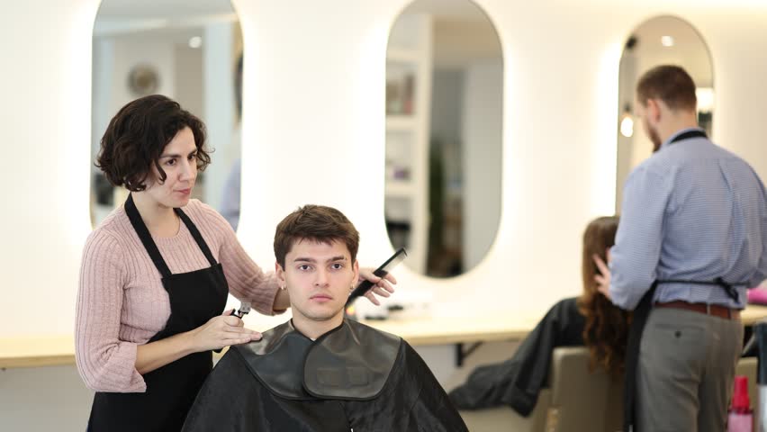 Young female hairdresser stylist gives haircut to young male client in beauty salon
