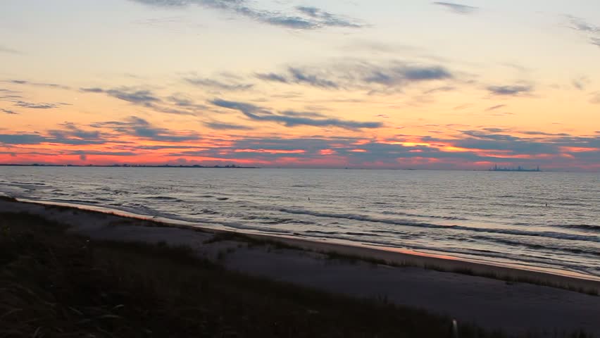 Sunset sky casts warm light over waves and beach, with distant Chicago skyline. Indiana Dunes National Park, USA