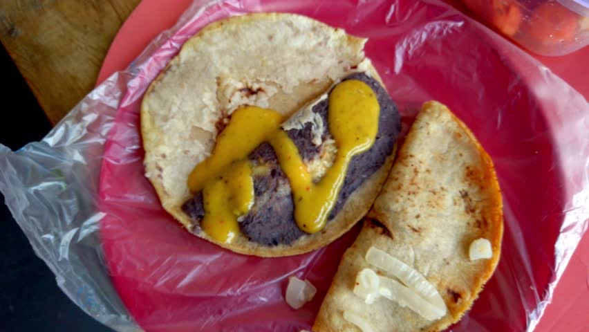 Wide shot of a taco with beans and yellow sauce served on a red plate.