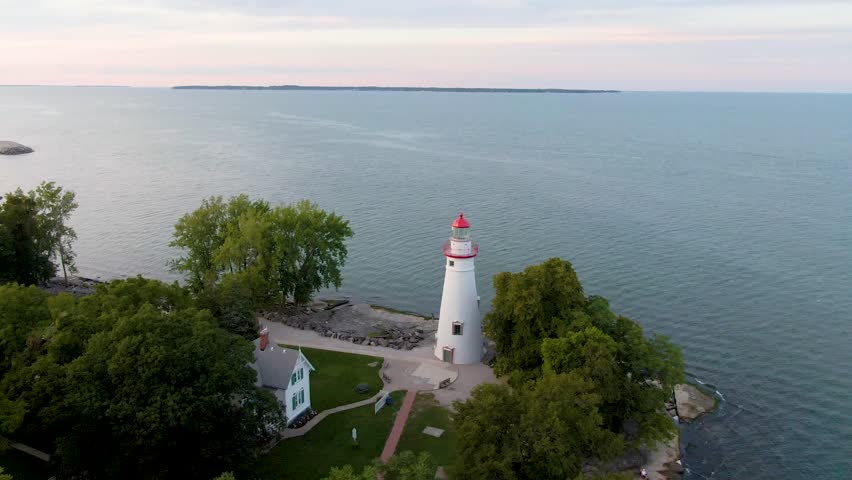 A point of interest drone shot of the Marblehead Lighthouse in Port Clinton, Ohio, at sunset. The blue and pink sky reflected off the water.