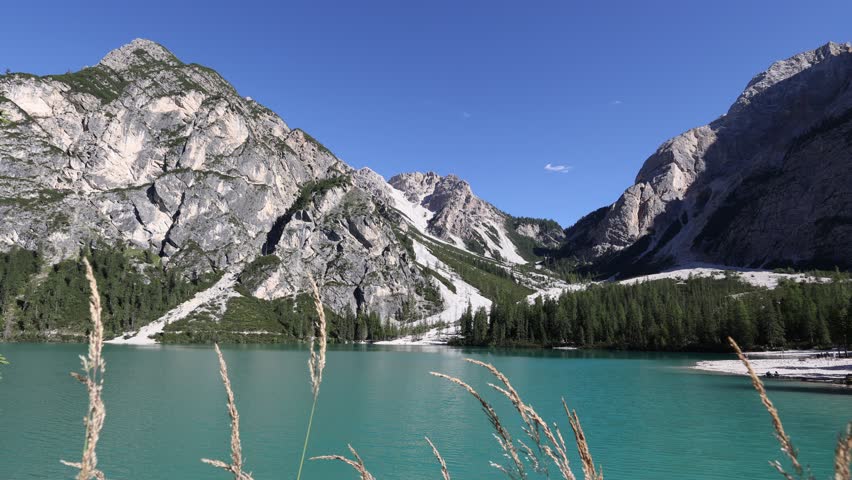 Breathtaking beauty of Pragser Wildsee, calm alpine lake Braies with emerald waters nestled amidst Dolomite mountains with towering rocky peaks on sunny summer day, Italy