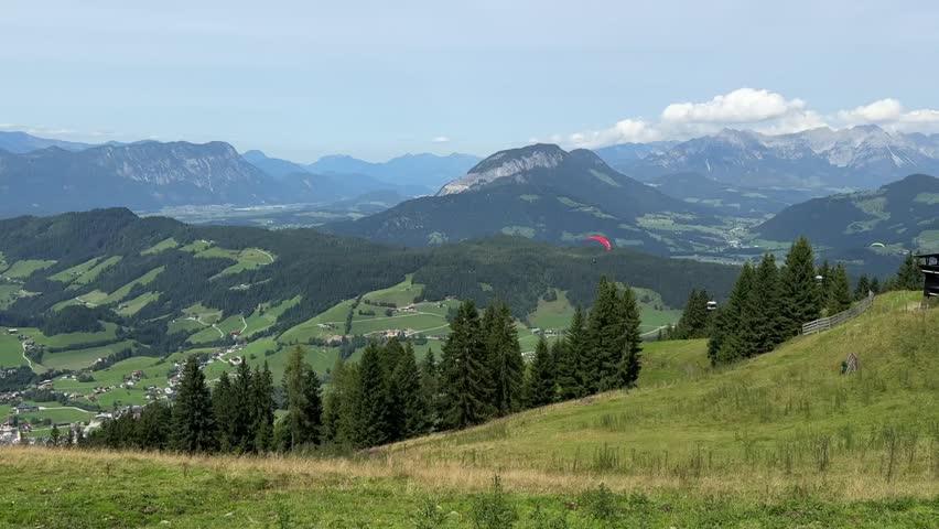 Majestic view of two paragliders against a mountain landscape. A red paraglider hovers in the air, while a blue one lifts off the ground and hovers, capturing the thrill of flight and adventure