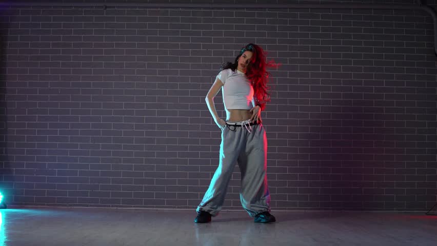 young crazy girl dancing hip hop against wall background in neon lighting, female choreographer moving to music and performing jazz funk in dance studio
