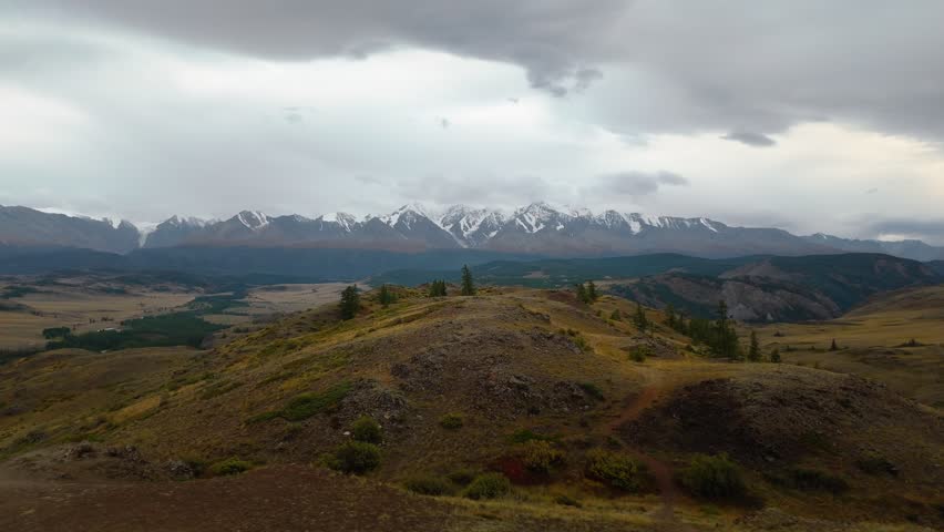 Aerial drone view of Mount Belukha in Altai Republic, Russia. Snow-capped peaks, valleys, and dramatic cloudy sky.