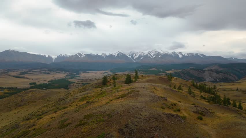 Aerial drone view of Mount Belukha in Altai Republic, Russia. Snow-capped peaks, valleys, and dramatic cloudy sky. Scenic wilderness landscape for travel, nature, and adventure themes.