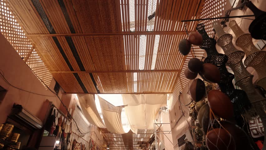 Wooden lattice roof and fabric canopies filter soft light above a traditional Moroccan market.