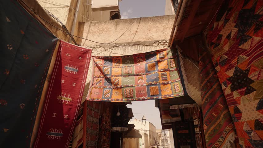 Brightly colored Moroccan rugs hang across a narrow alleyway in a traditional market.