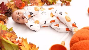 Baby wearing Halloween pajamas trying to roll over on a white blanket surrounded by a garland of dried leaves, pine cones, and pumpkins - Powered by Shutterstock - Get 15% off with code: PIKWIZARD15