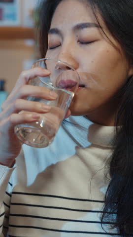 Vertical Screen : Sick young Asia woman holding pill glass of water take medicine sit on couch at home night. Girl taking medicine after doctor order, quarantine at house, social distancing concept.