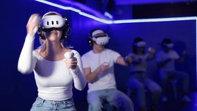 In darkened hall of gaming club, girl in VR helmet takes part in group game. Player overcomes obstacles and reaches goal in parallel reality. Imaginary fantastic world  - Powered by Shutterstock - Get 15% off with code: PIKWIZARD15