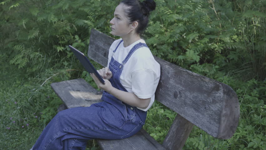 Cute woman is relaxing in the park on bench with tablet PC
