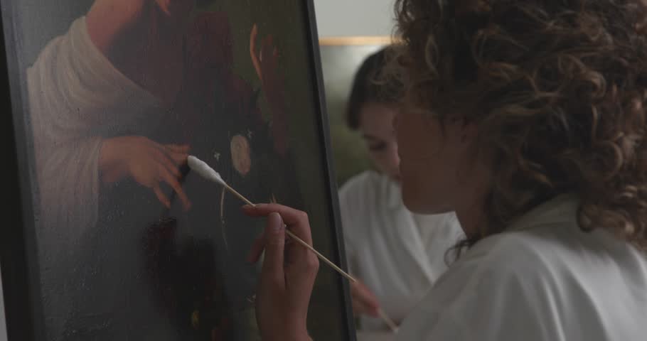 Painting conservator working in the laboratory, she is cleaning a Caravaggio oil painting using a cotton swab, art conservation concept