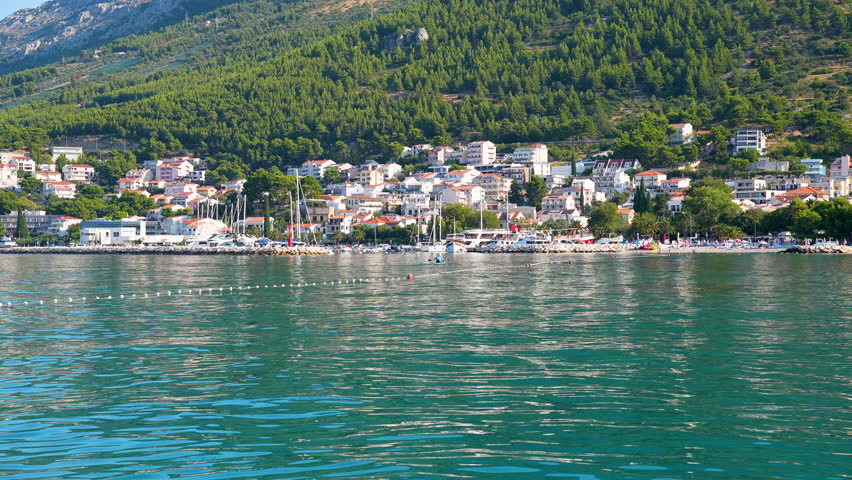 Charming Mediterranean Croatian Seaside Village: A Beautiful Harbor Filled with Yachts and Lively Beach, Set Against Backdrop of Steep Mountains and Verdant Forests, Ideal for Tourism and Relaxation